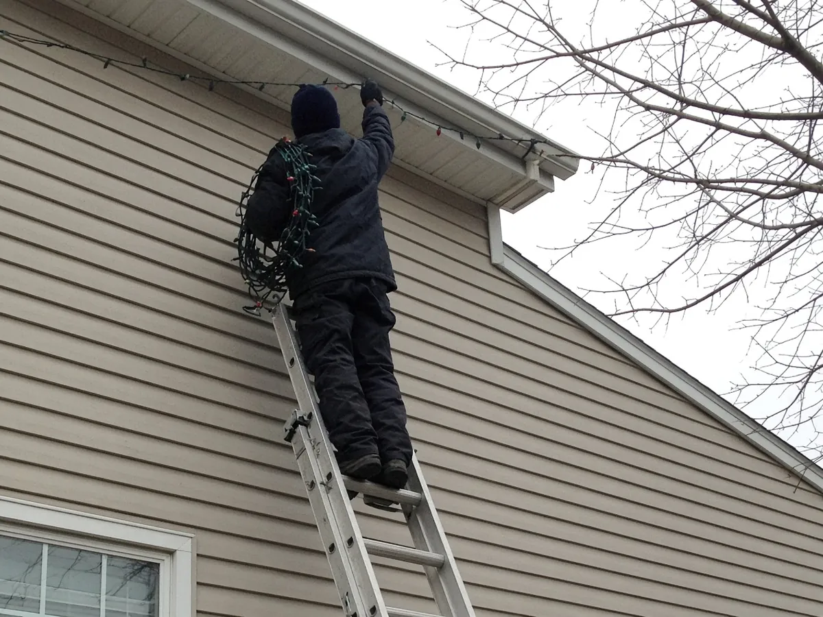 Installer on a ladder clipping holiday lights to a gutter